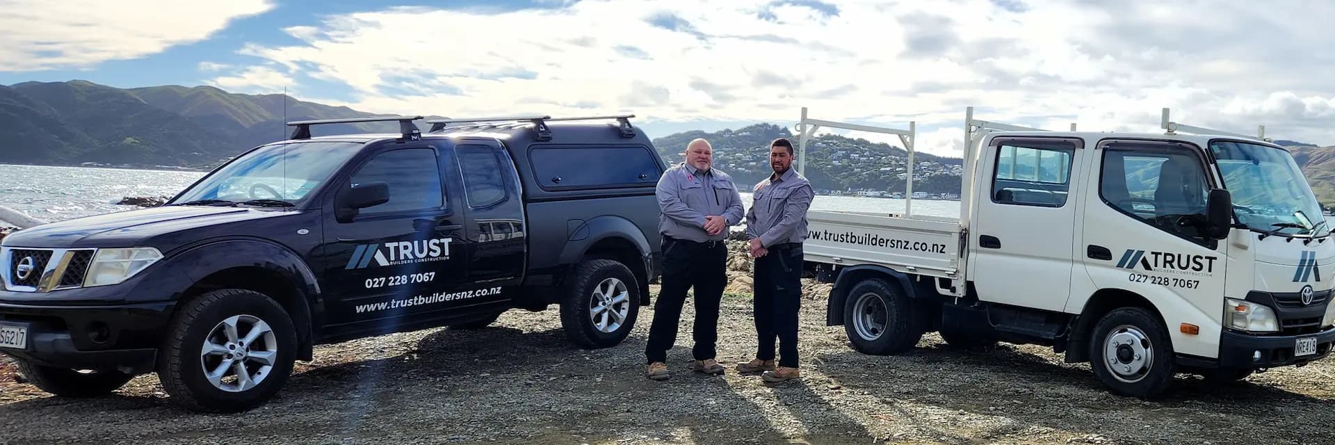 Trust Builders Construction team standing with company vehicles by the Wellington coast